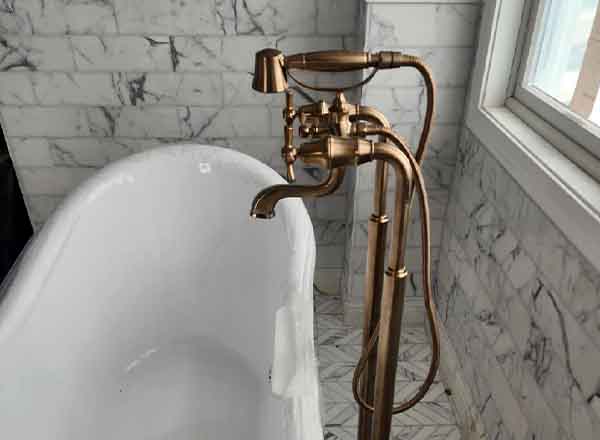 Bathroom remodeling project featuring freestanding tub with bronze faucet and marble tile walls in South Jersey home.